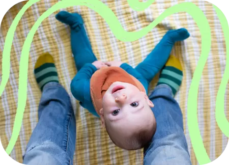 A happy baby is sitting and looking up at the camera.
