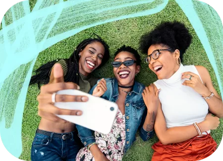 Three friends are lying on the grass and taking a selfie.