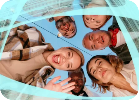 Group of happy friends standing in a circle outdoors, viewed from below against a clear blue sky with visible clothing details like plaid and jackets.