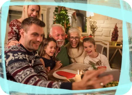 Family gathered around a festive dinner table decorated with candles and holiday ornaments, with a Christmas tree in the background.