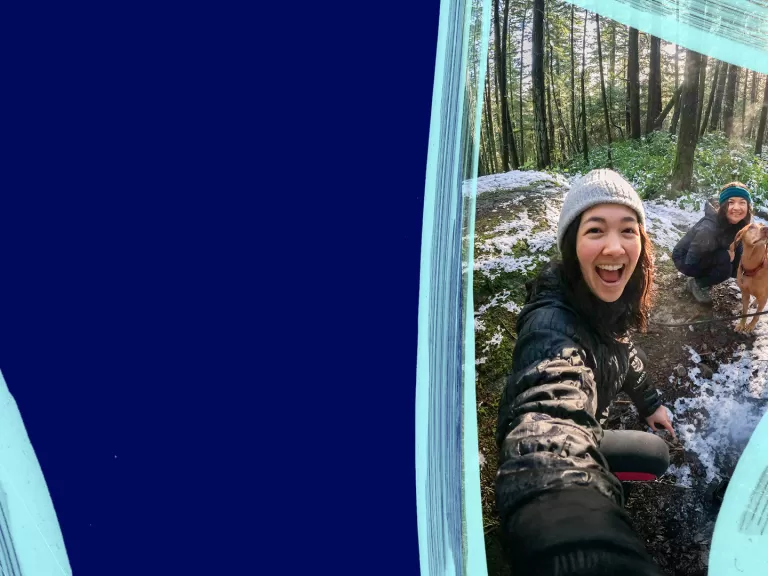 Three happy friends on a forest trail with patches of snow, standing near a tan dog on a leash among tall trees.