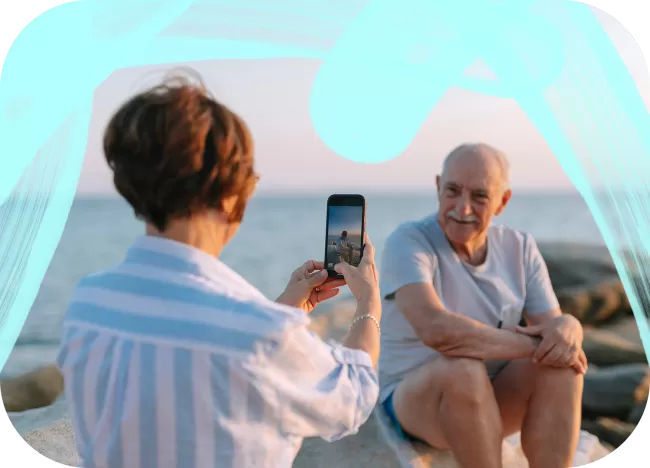 A woman is taking a picture of a man on the beach.