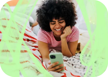 A young woman is lying down on a picnic blanket and is watching something on her phone.