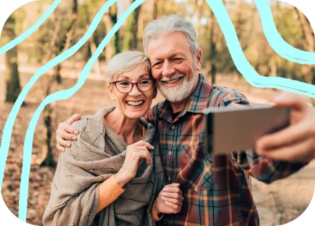 An older couple is taking a selfie in a park.